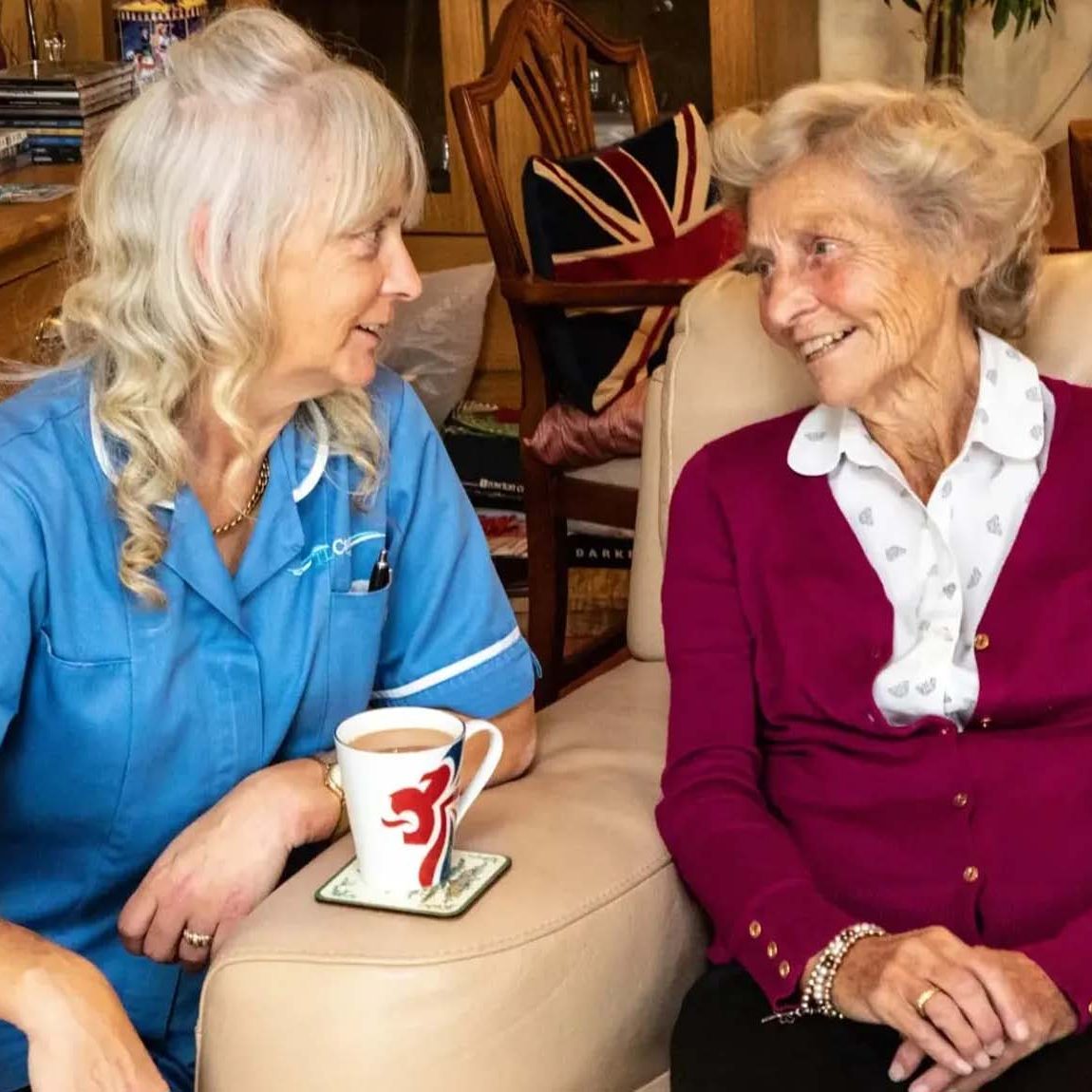 Carer helping old woman with cup of tea